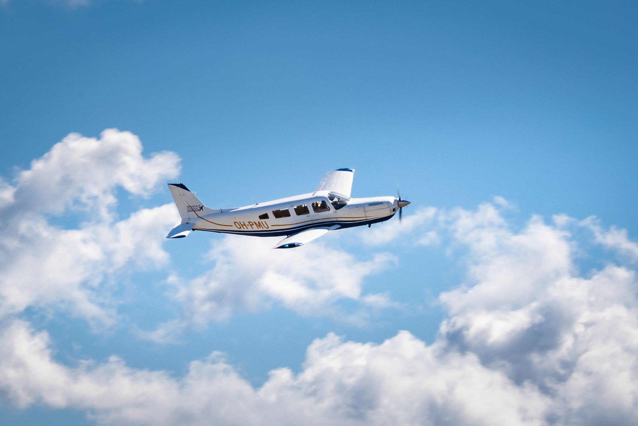 Piper PA-32R -pienlentokone lentämässä sinisellä taivaalla pilvien yläpuolella.